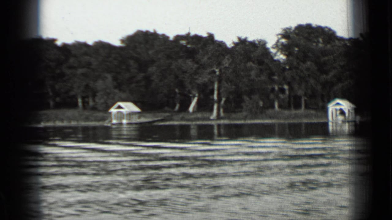 Rippled lake water with a wooded shore and small white boathouses in the distance.