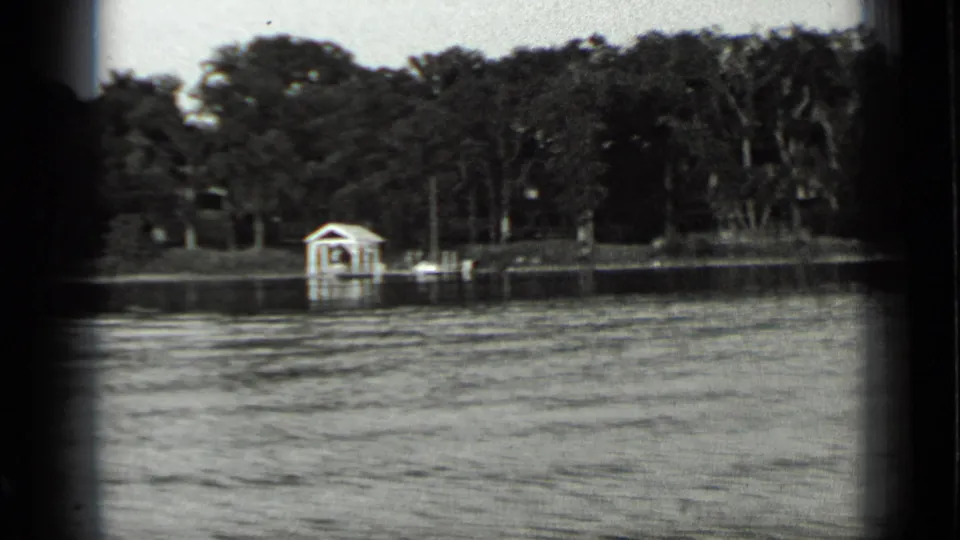 Clear Lake, California, 1939 frame centered on a white boathouse along a wooded shore, filmed from across the water.