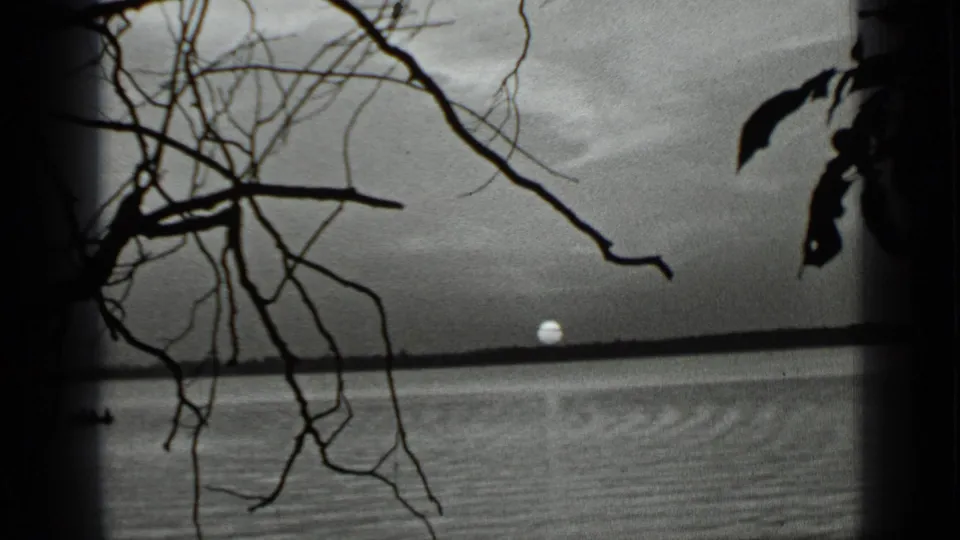 1939 Clear Lake view with the sun low on the horizon, calm water, silhouetted branches, and dark 8mm frame edges.
