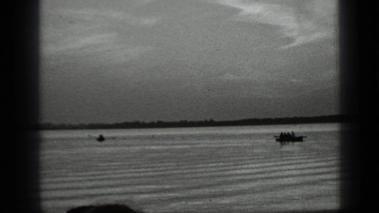 Small boats on calm lake water with a distant shoreline and cloudy sky.