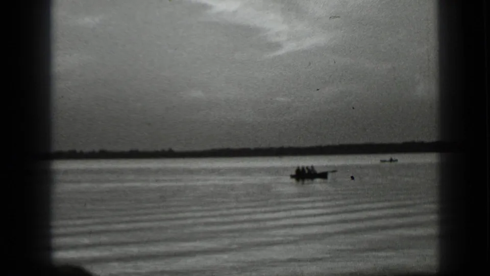 Home-movie view of a small passenger boat on Clear Lake with ripples, a distant shore, and another craft behind it.