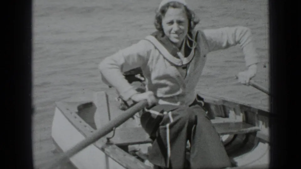 Adult woman in a sailor-style top rows a small boat on Clear Lake, California, smiling toward the camera in 1939 home-movie footage.