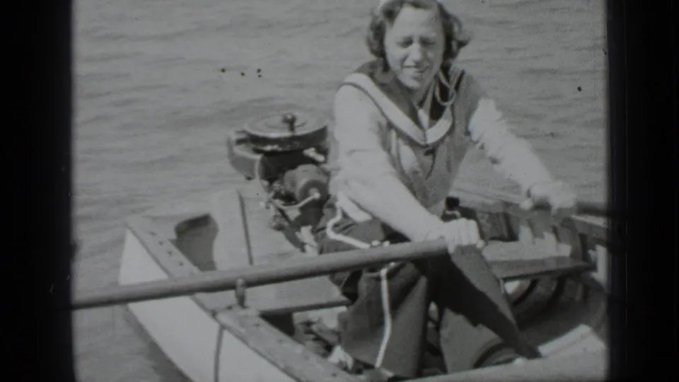 Close 1939 Clear Lake home-movie frame of an adult woman rowing a small boat, with lake water and a motor at the stern.