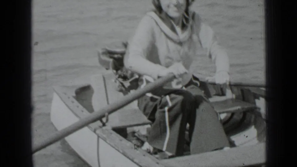 Adult woman in a sailor-style outfit continues rowing on Clear Lake in a soft, grainy 1939 8mm home-movie frame.