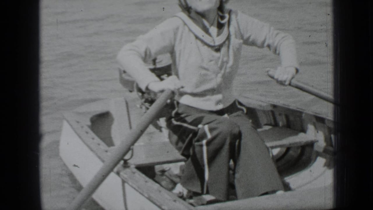 Woman in a small rowboat holds oars on calm lake water.