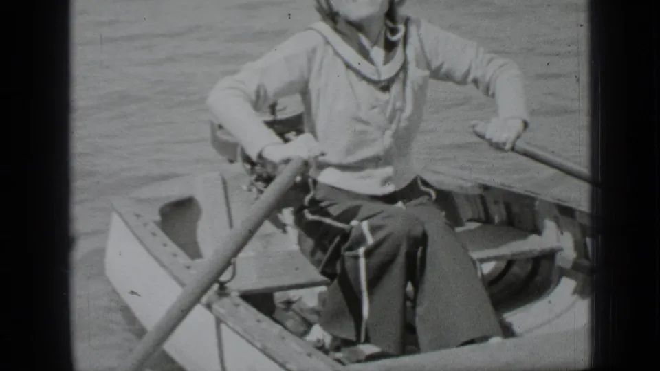In 1939 Clear Lake footage, a woman in a sailor-style top rows a small boat across calm water.