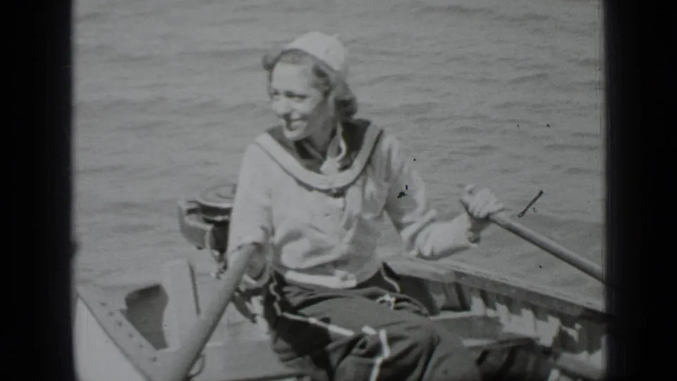 The woman continues rowing on Clear Lake, smiling as the small boat sits low in calm water.