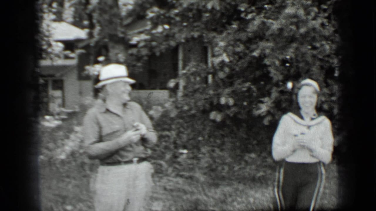 A man in a brimmed hat stands opposite a woman in a sailor-collar sweater in the Clear Lake garden setting.