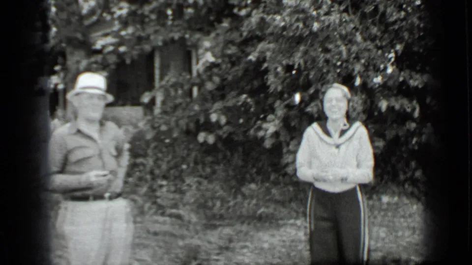 The man in a brimmed hat and the woman in a light sailor-collar sweater stand in the Clear Lake garden, facing the camera area.