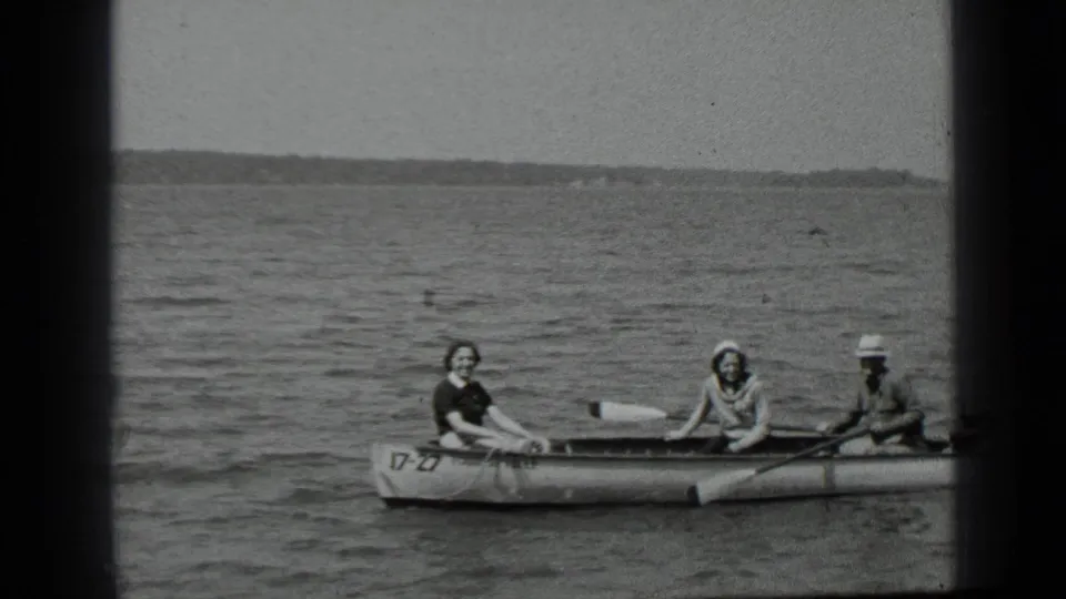 1939 Clear Lake home-movie frame showing three people in a rowboat on open water, with a distant shoreline behind them.