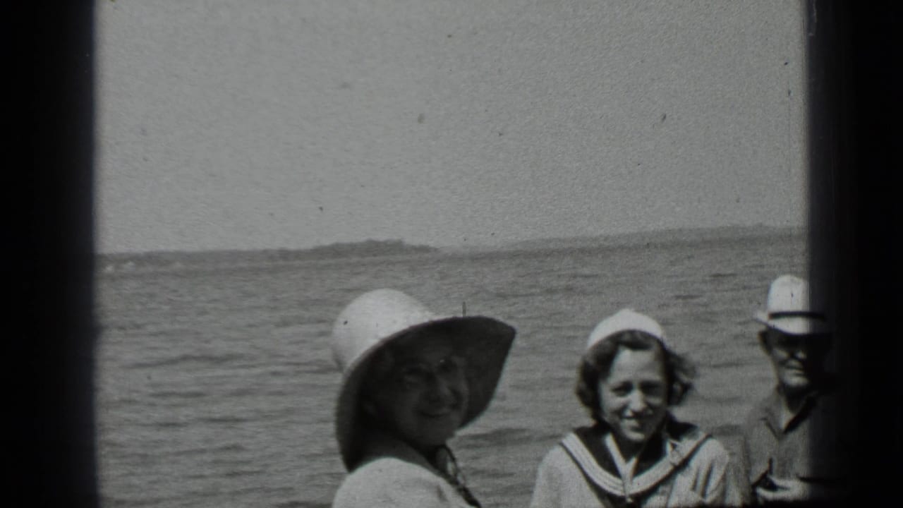 People in hats and a young person in a sailor-style outfit stand near the lake.
