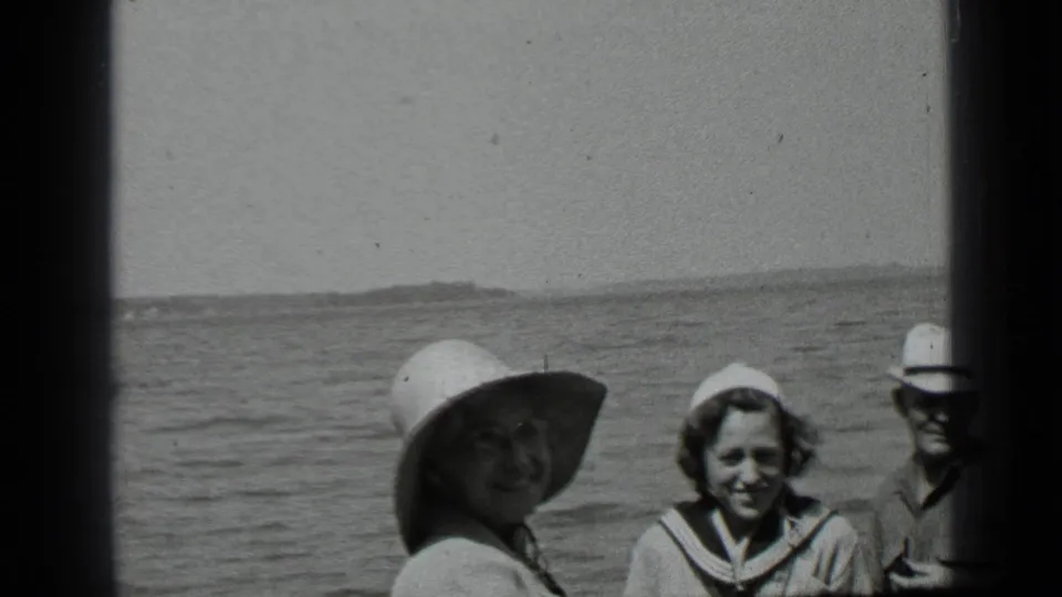 Close home-movie view at Clear Lake showing smiling family members near the water, including a wide-brimmed hat and sailor-style collar.