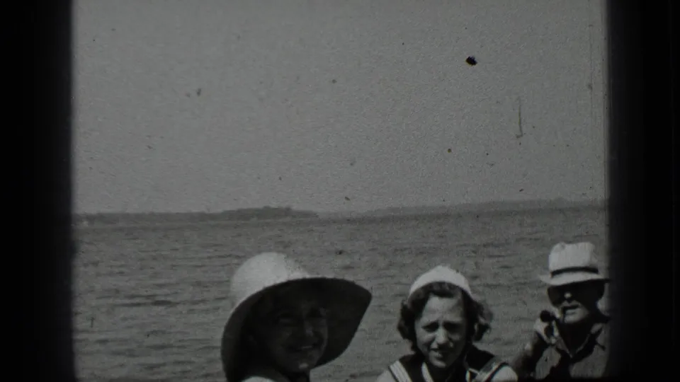 Close 1939 Clear Lake home-movie frame showing three family members posing together, with hats, lake water, and shoreline visible.