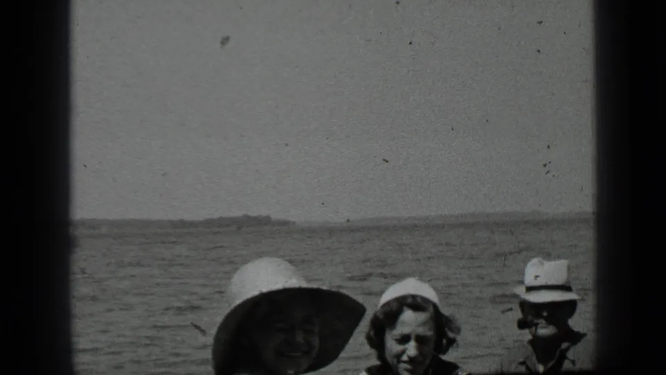 Clear Lake home-movie frame from 1939 showing three adults in hats near the water, with the distant shoreline behind them.