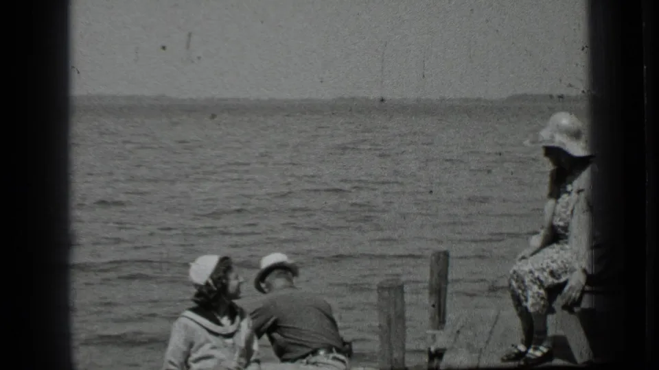 A 1939 Clear Lake home-movie frame shows adults gathered on a wooden dock, with one person seated at the right and others near the water.