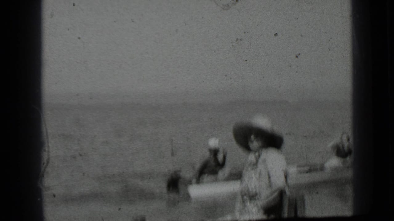 A small boat passes near a seated woman in a wide-brimmed hat.