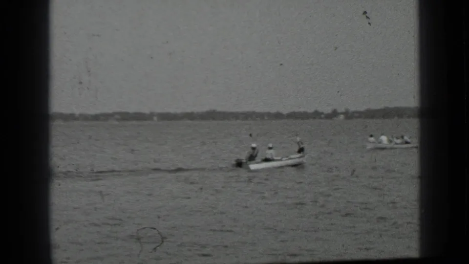 Two small boats with passengers travel across Clear Lake, with rippled water and a low shoreline in the distance.