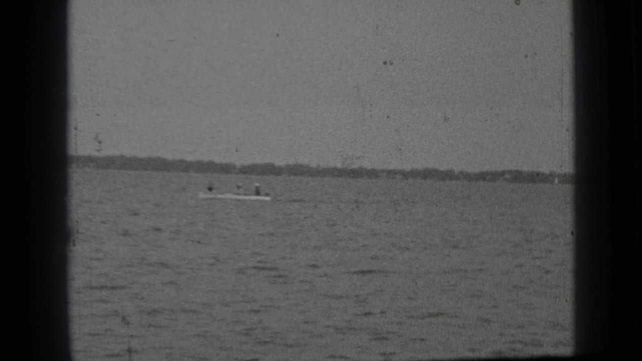 Small motorboat with riders crossing a rippled lake near a distant shoreline.