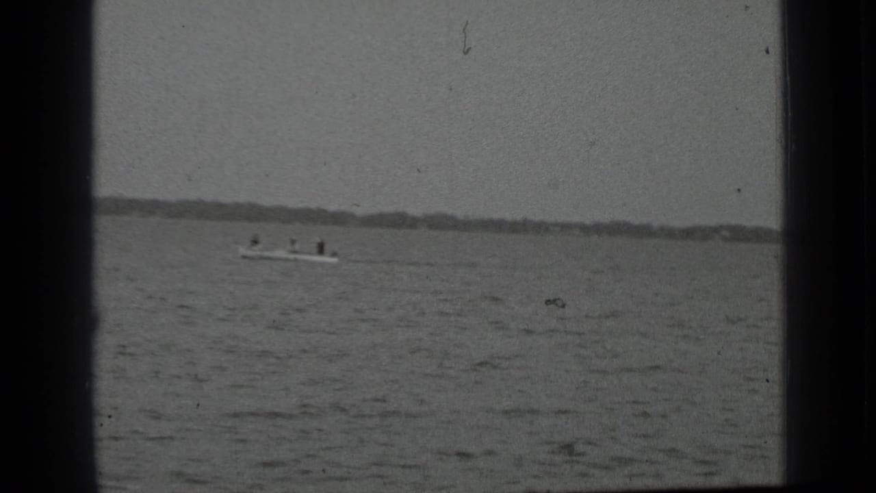 Motorboat with several riders on open water, framed by dark 8mm film borders.