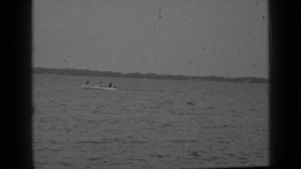 Small motorboat carrying people across Clear Lake, California, seen at a distance in black-and-white 8mm footage.