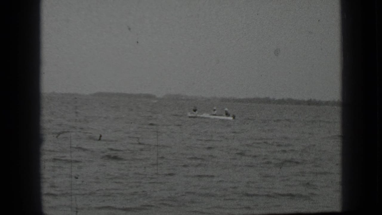 Small boat with people on open lake water beneath a distant shoreline.