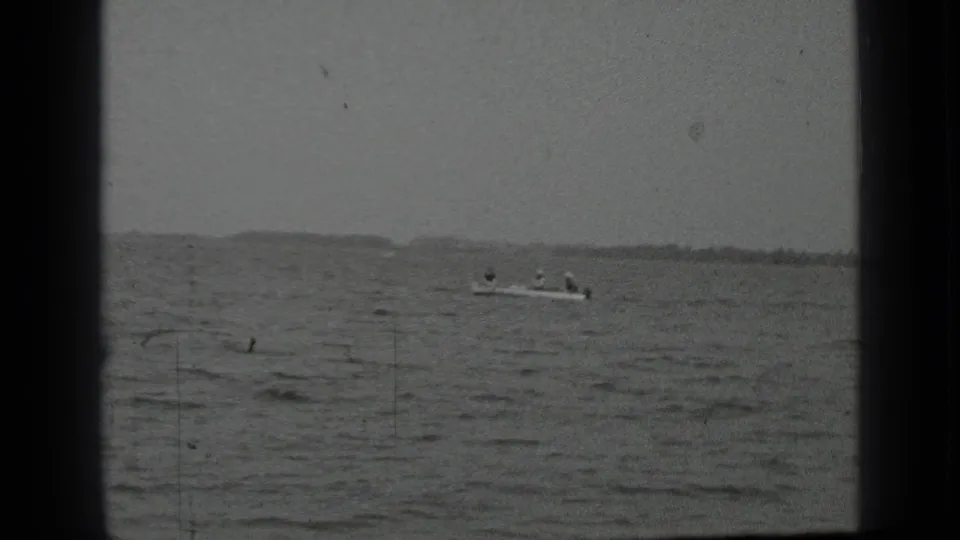 1939 Clear Lake home-movie frame showing a small boat carrying people across broad, choppy water with a low shoreline beyond.