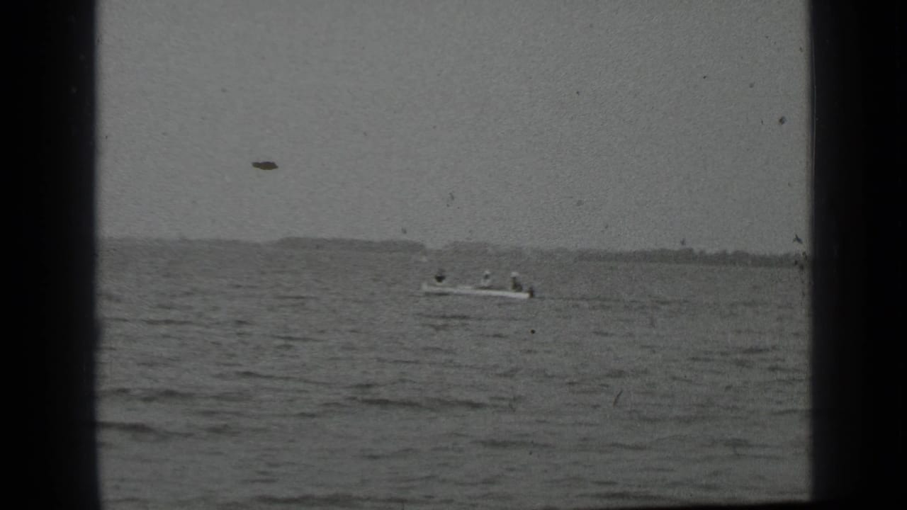 Small boat on a lake, framed by dark film borders and distant land.