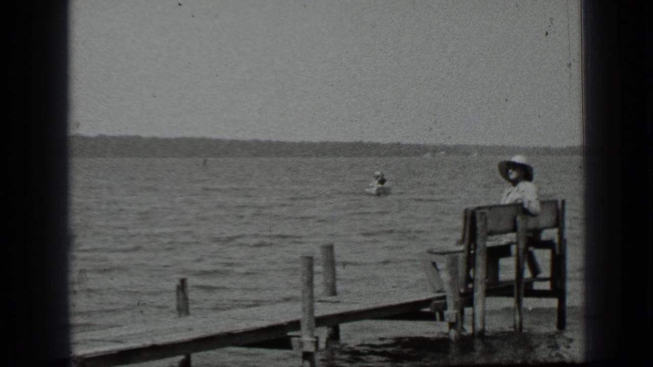 Woman seated on a dockside bench as a canoe moves across the lake behind her.