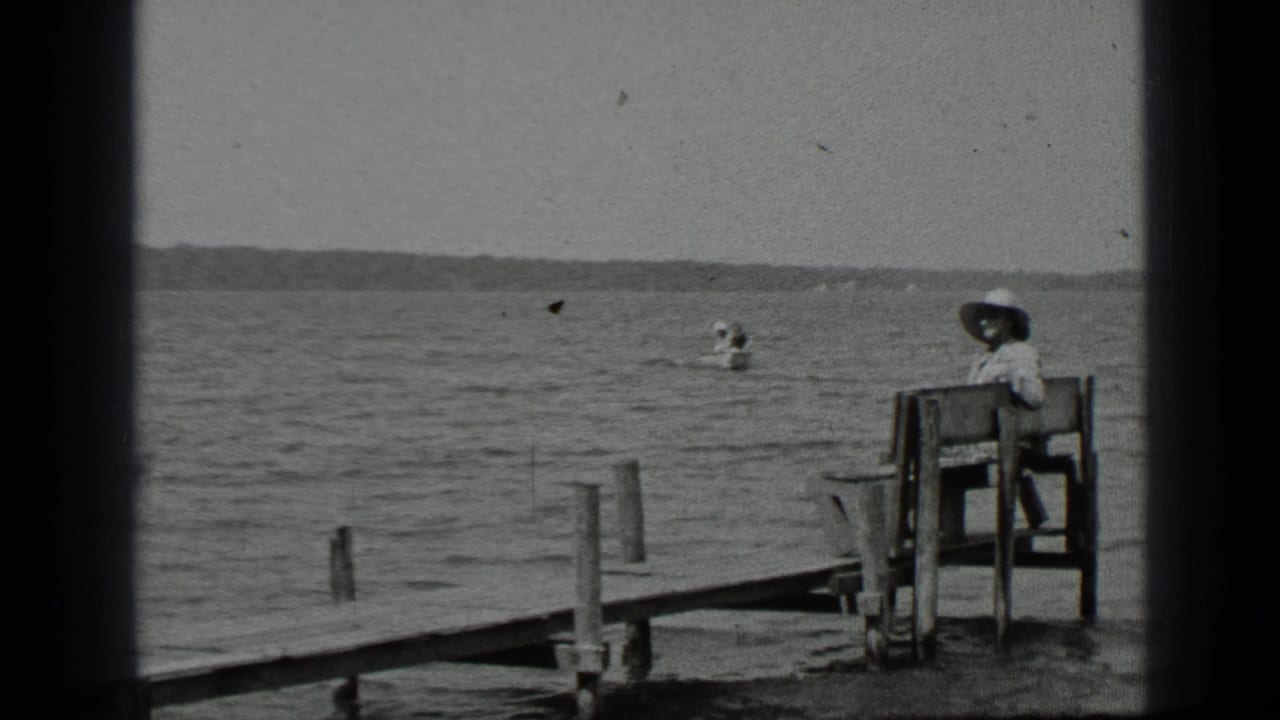 Woman seated beside the lake with a small canoe visible farther out on the water.