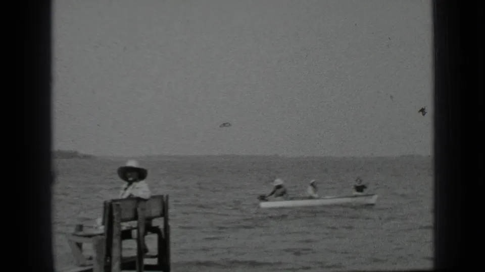 A 1939 Clear Lake frame shows people in a canoe traveling behind a woman seated on a bench at the edge of the dock.