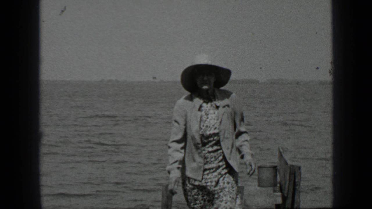 Woman in a wide-brimmed hat walking near lake water and a dock edge.