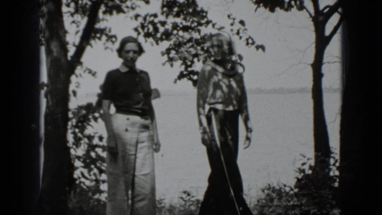 Two women standing by trees with lake water in the background.
