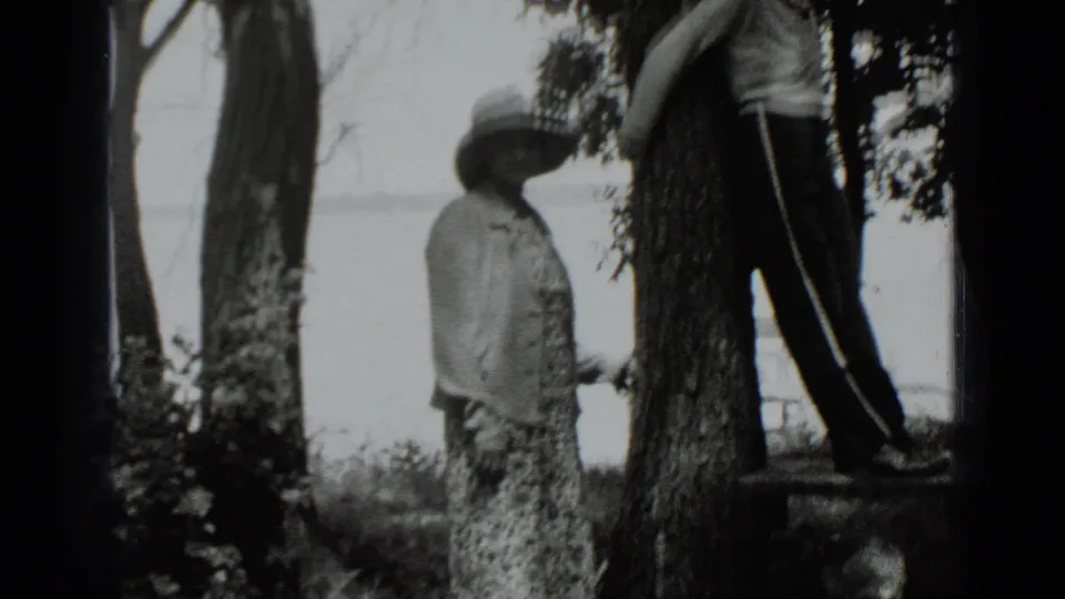 Soft 8mm frame from Clear Lake in 1939 showing a girl standing near a tree with a boy partly cropped at the right edge.