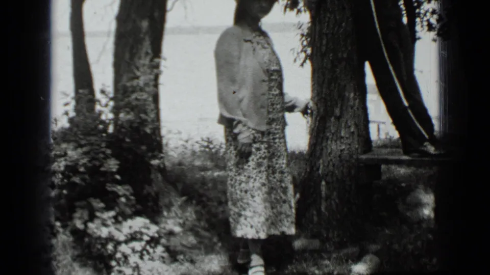 Clear Lake 1939 home-movie frame showing a girl beside a tree and a boy leaning at the right edge with water behind them.