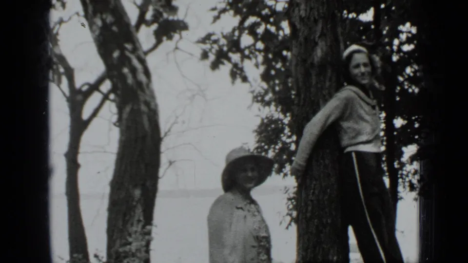 A 1939 Clear Lake home-movie frame shows two women in a wooded lakeside yard, with one woman smiling at the camera.