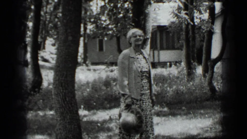At Clear Lake in 1939, a woman stands in a shaded yard holding a round object, with a small house or cabin in the background.