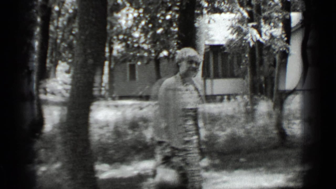 Soft, slightly blurred view of the woman standing by trees with a house behind.