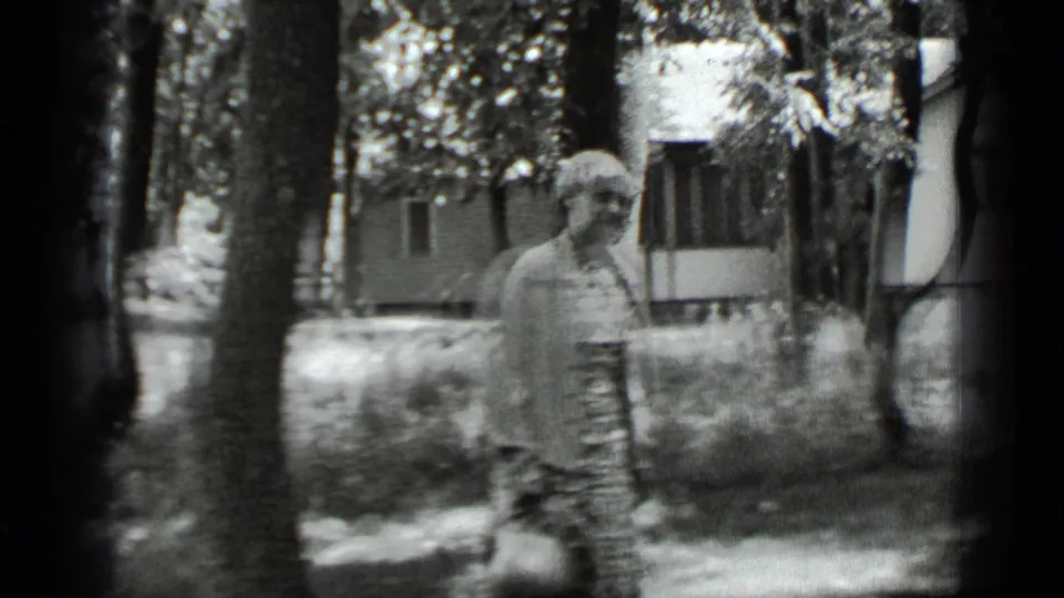 The woman remains in the wooded Clear Lake setting, partially softened by motion blur and 8mm film grain.