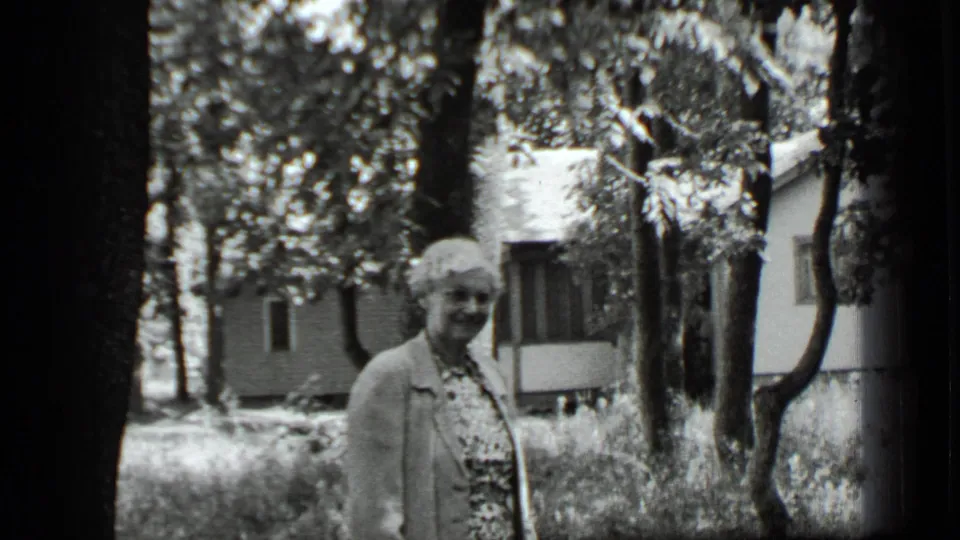 A closer 1939 frame shows the smiling woman in a patterned dress and jacket, with trees and a house in the background.