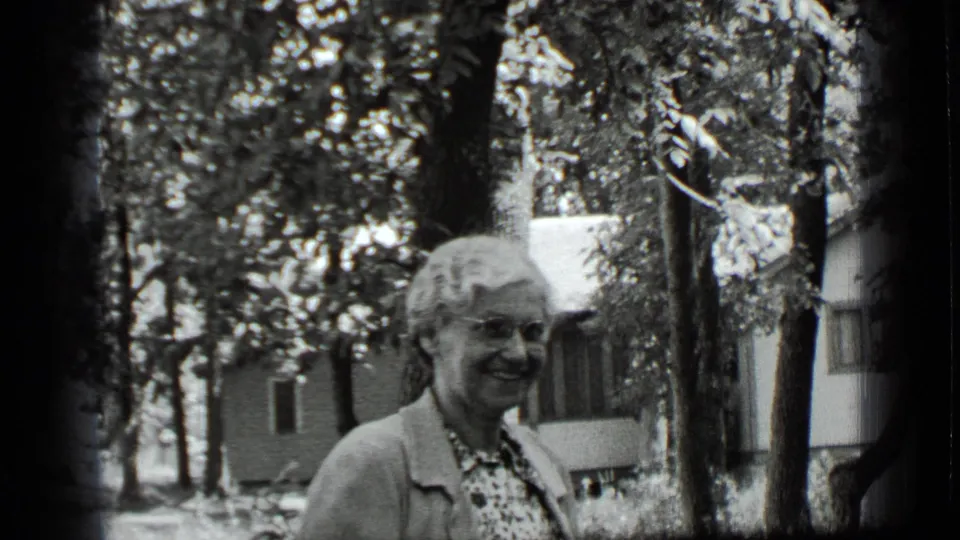 Older woman smiles broadly in a shaded residential yard in Clear Lake, California, with trees and a house behind her.