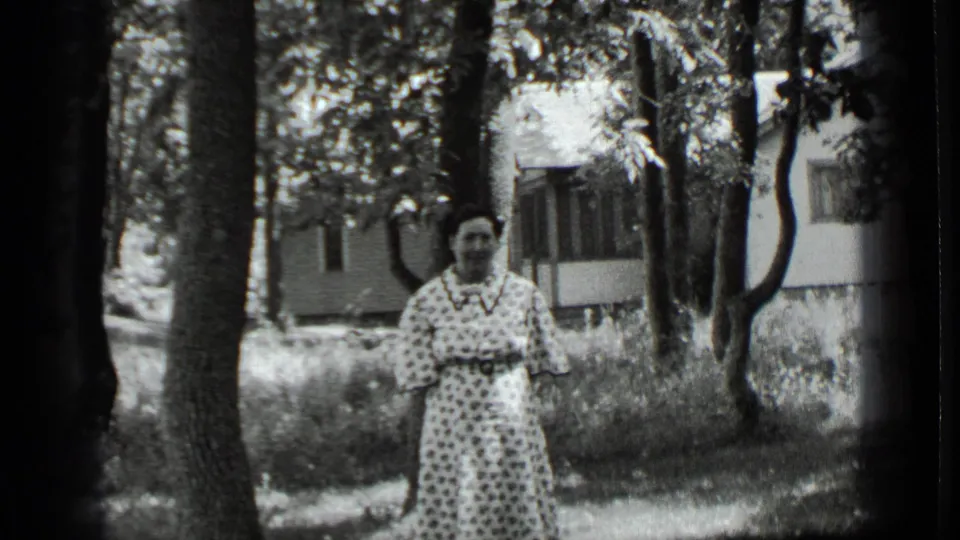 The woman remains posed outdoors at Clear Lake, framed by trees and a house in the background.