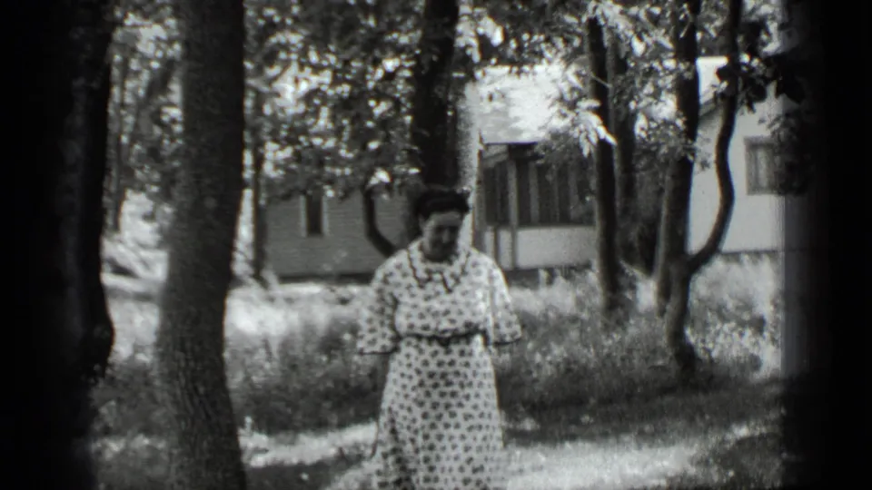 The woman looks down in the wooded Clear Lake setting, with the house and sunlit grass still visible behind her.