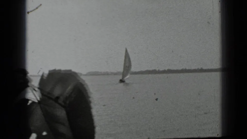 1939 Clear Lake, California 8mm frame with a distant sailboat on open water and a dark foreground obstruction at left.