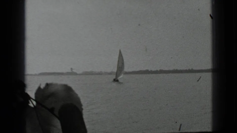 1939 Clear Lake, California frame showing a small sailboat against a low shoreline, with 8mm gate shadows and surface wear.