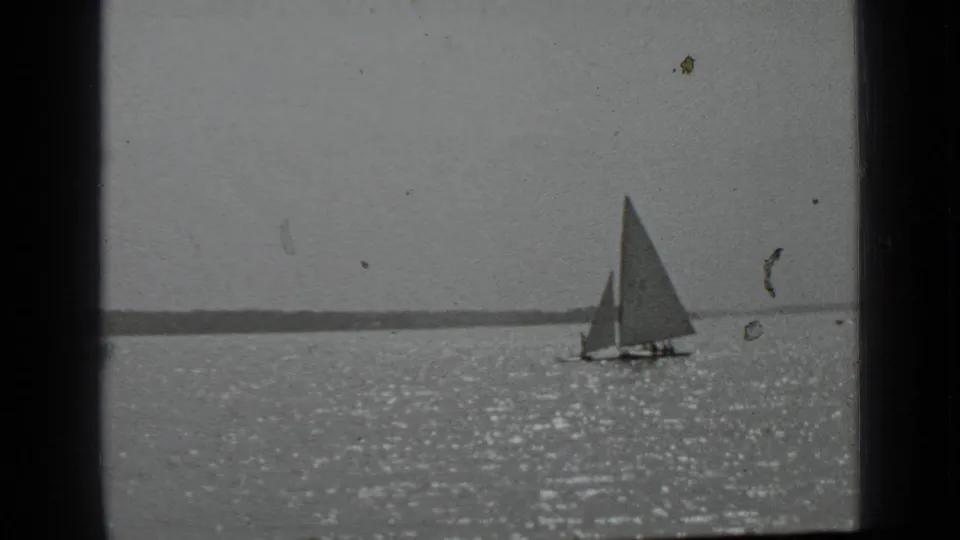 1939 Clear Lake, California 8mm frame with a sailboat on sparkling water and a low shoreline in the background.