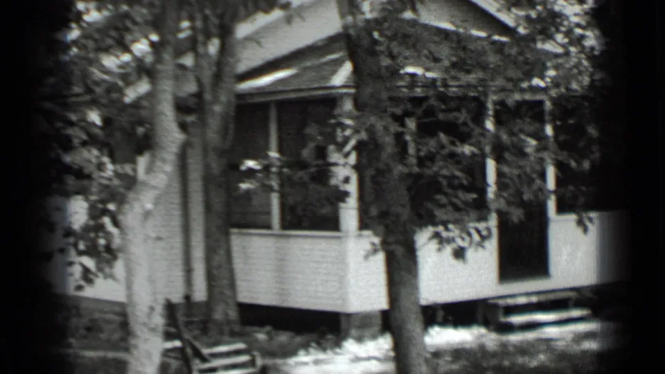 Clear Lake 1939 home-movie still showing a white porch facade, dark doorway, trees, and sunlit yard patches.