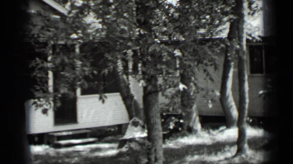 1939 Clear Lake home-movie frame showing a white wooden house behind tree trunks and leafy branches.