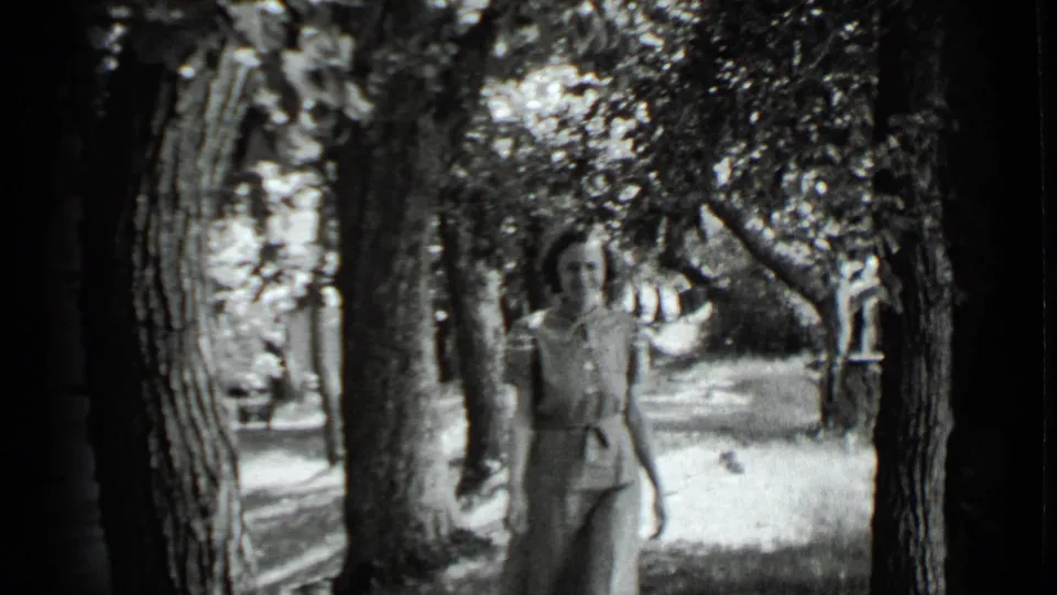 A woman in a light dress walks through trees near a house in 1939 Clear Lake home-movie footage.