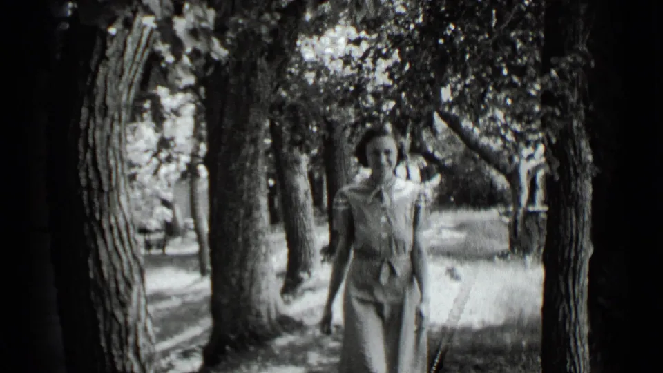 Adult woman in a light patterned dress walks toward the camera among trees at Clear Lake, California, in 1939.