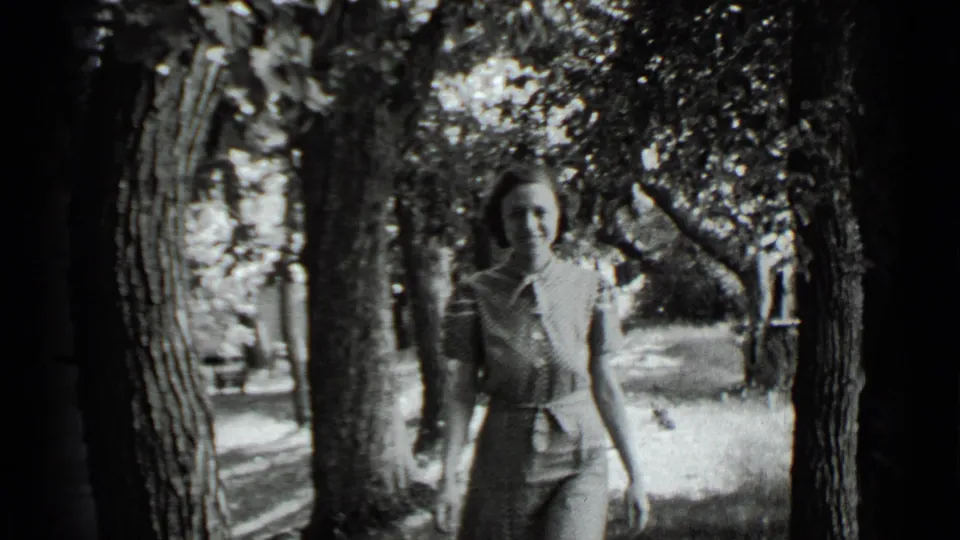 Adult woman approaches the camera in a wooded Clear Lake setting, wearing a belted light dress in 1939 home-movie footage.